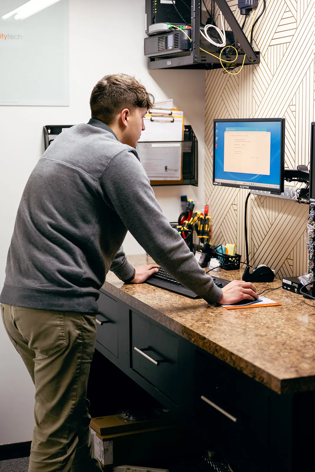 An IT technician standing at a desk, working on a computer.